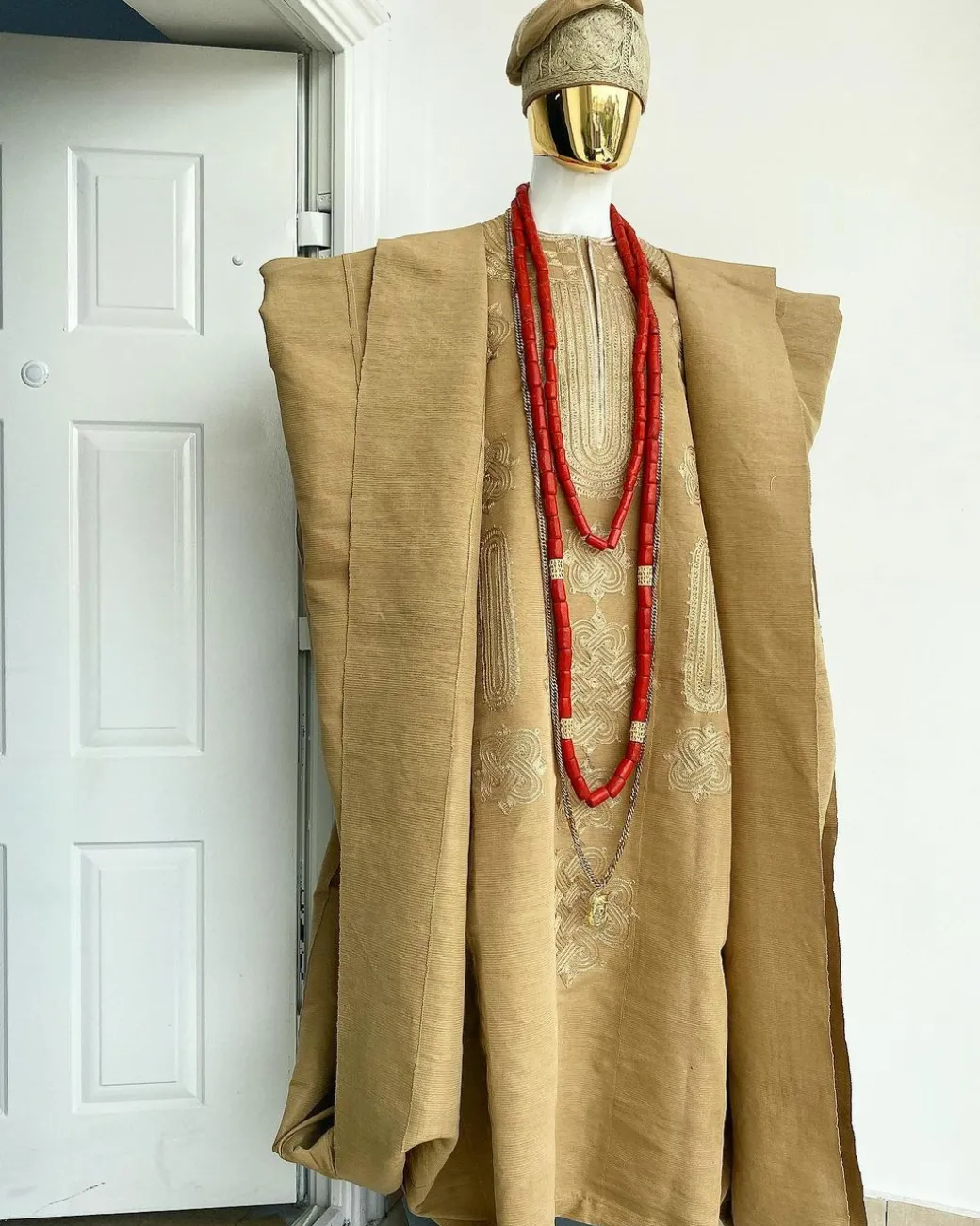 A champagne gold aso oke regal agbada, dashiki, sokoto, red and gold mix coral bead, matching hand woven Yoruba hat, and a long gold chain with a Jesus piece.