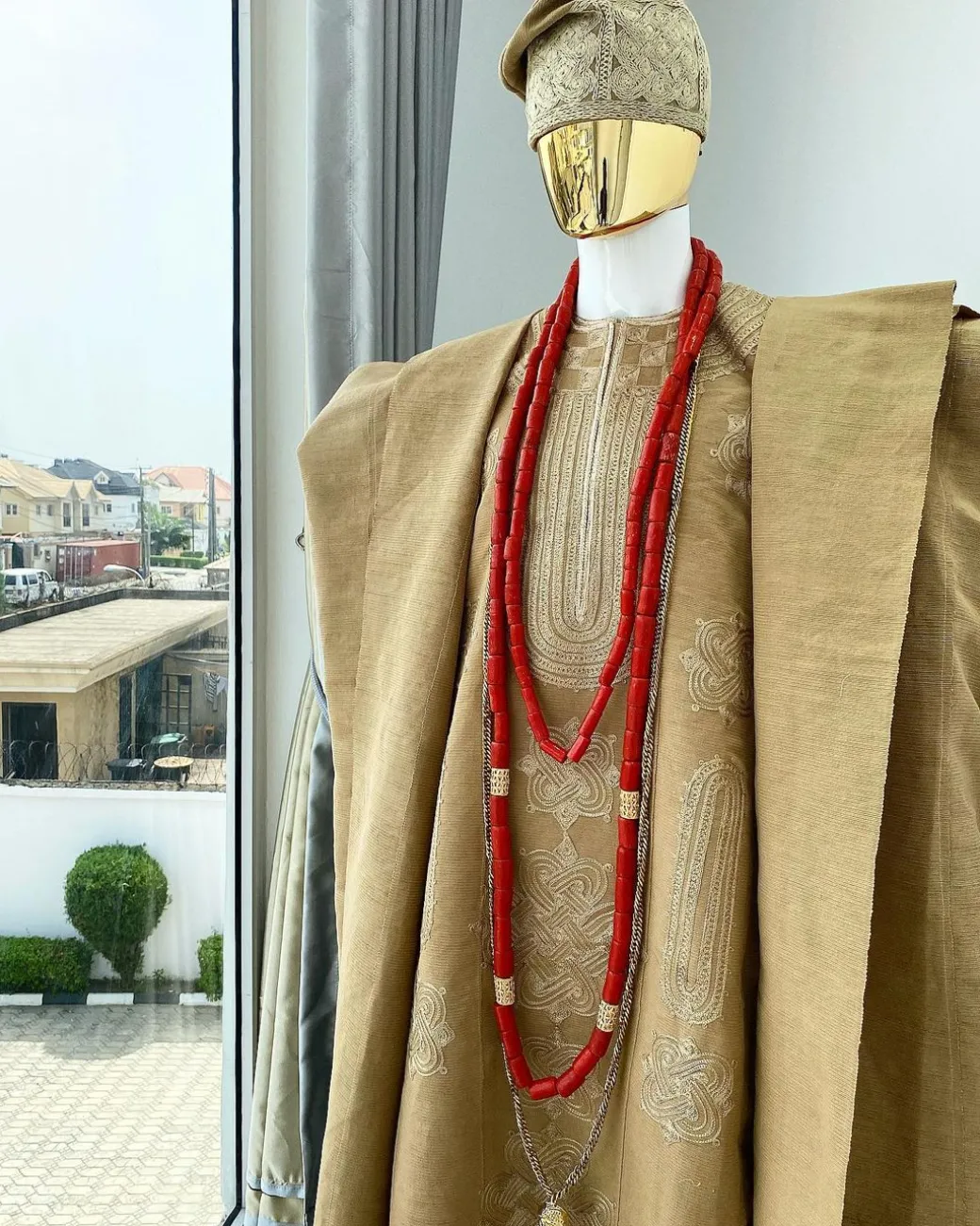 A champagne gold aso oke regal agbada, dashiki, sokoto, red and gold mix coral bead, matching hand woven Yoruba hat, and a long gold chain with a Jesus piece.